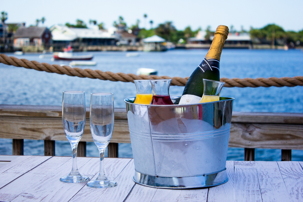 Bucket_of_Bubbles_20220412 - 005 Example of Food Photography for DoorDash, Uber Eats, Grub Hub, and any food delivery service app. Food Photo is of champaign chilling in a metal ice bucket. We are located outside with water and boats behind the beverages. There also wine glsses to the side of the bucket. The oicture is a profile shot showcasing the bveerages by the water.