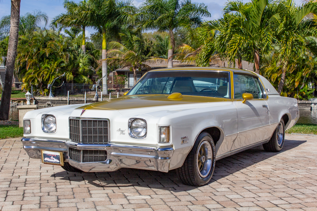 GM_Grand_Prix_20230210 (59)comp Example of Automotive Photography. Car Photography and Videography for Bring-a-Trailer, Auto Hunter, Barn Finder, Auto Trader, and any car and automobile sales sites. Car Photo is of a white and gold GM Grand Prix . The camera is positioned in the driver's side front of the vehicle showing the car from the exterior. It has palm trees and a bay of water in the background.