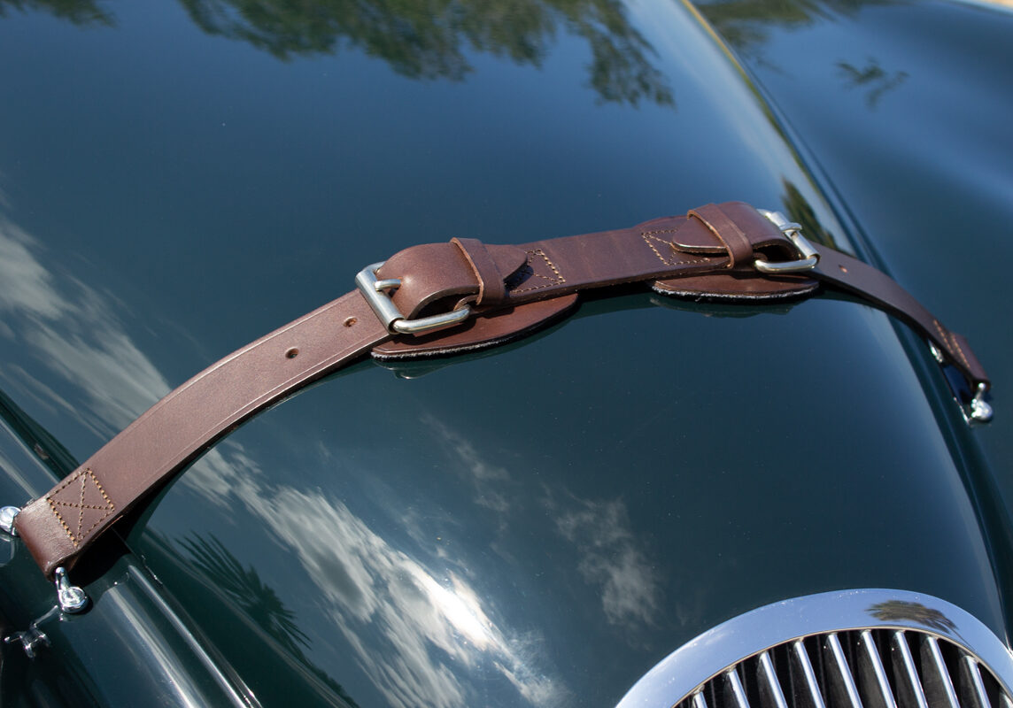 1953_Jaguar_XK120_20230520 (113)comp Example of Automotive Photography. Car Photography and Videography for Bring-a-Trailer, Auto Hunter, Barn Finder, Auto Trader, and any car and automobile sales sites. Car Photo is of the leather strap on the hood of a green 1953 Jaguar XK120
