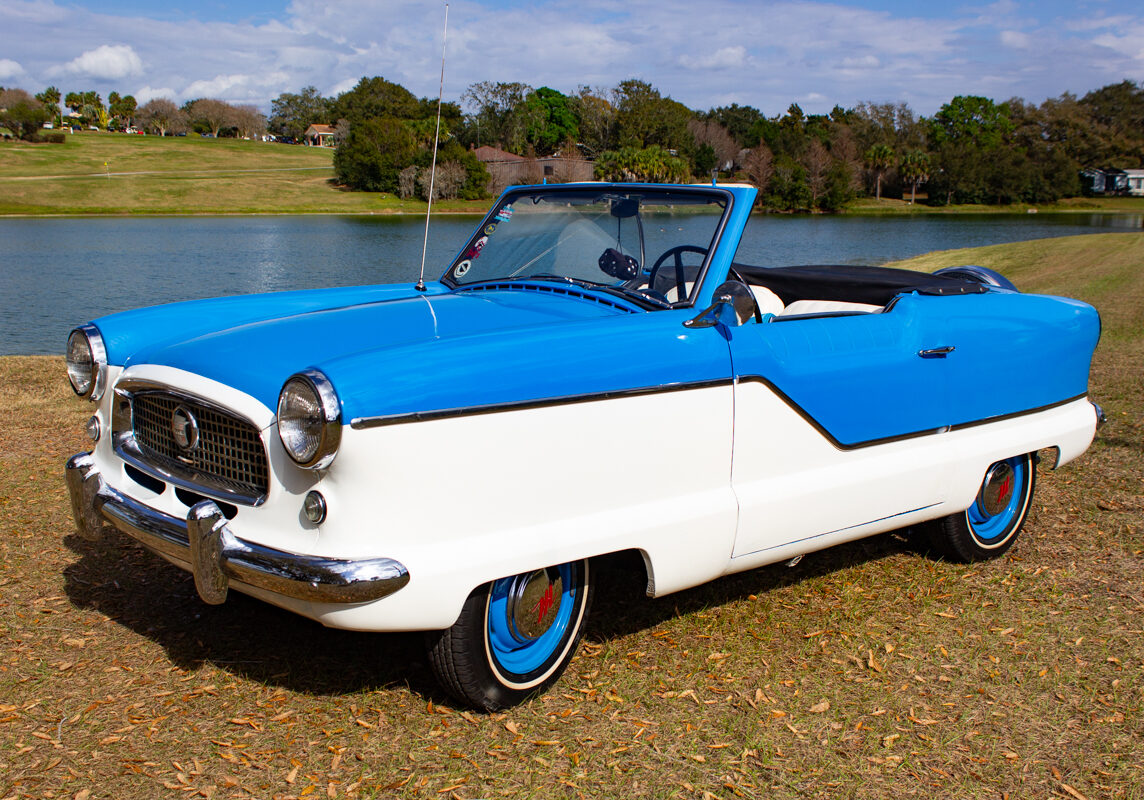 1956_Nash_Metropolitan_20230210 (7)comp Example of Automotive Photography. Car Photography and Videography for Bring-a-Trailer, Auto Hunter, Barn Finder, Auto Trader, and any car and automobile sales sites. Car Photo is of the exterior of a bue and white 1965 Nash Metropolitan. The photo is taken from the drivers side front and features a lake in the background.