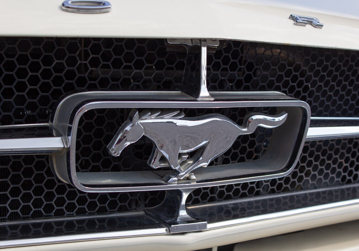 1965_Ford_Mustang_Convertible_20230630 (82)comp Example of Automotive Photography. Car Photography and Videography for Bring-a-Trailer, Auto Hunter, Barn Finder, Auto Trader, and any car and automobile sales sites. Car Photo is of the front grill chrome logo of a Mustang from the 1965 Ford Mustang convertible that is cream colored.