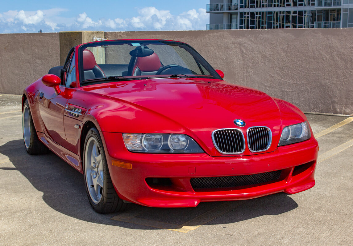 2000_BMW_M_Roadster_20230617 - (5)comp Example of Automotive Photography. Car Photography and Videography for Bring-a-Trailer, Auto Hunter, Barn Finder, Auto Trader, and any car and automobile sales sites. Car Photo is of the exterior of a fire engine red 2000 BMW Roadster convertible on the rooftop of a parking garage. We see the sky and part of the city of St. Petersburg, Florida in the background.