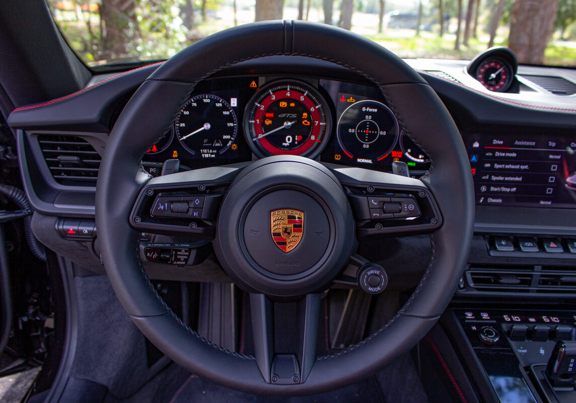 2022_Porsche_911_Carrera_GTS_20230102 - (162)comp Example of Automotive Photography. Car Photography and Videography for Bring-a-Trailer, Auto Hunter, Barn Finder, Auto Trader, and any car and automobile sales sites. Car Photo is of the driver's view of the steering wheel of a 2022 Porsche 911. The steering wheel is black with red details.