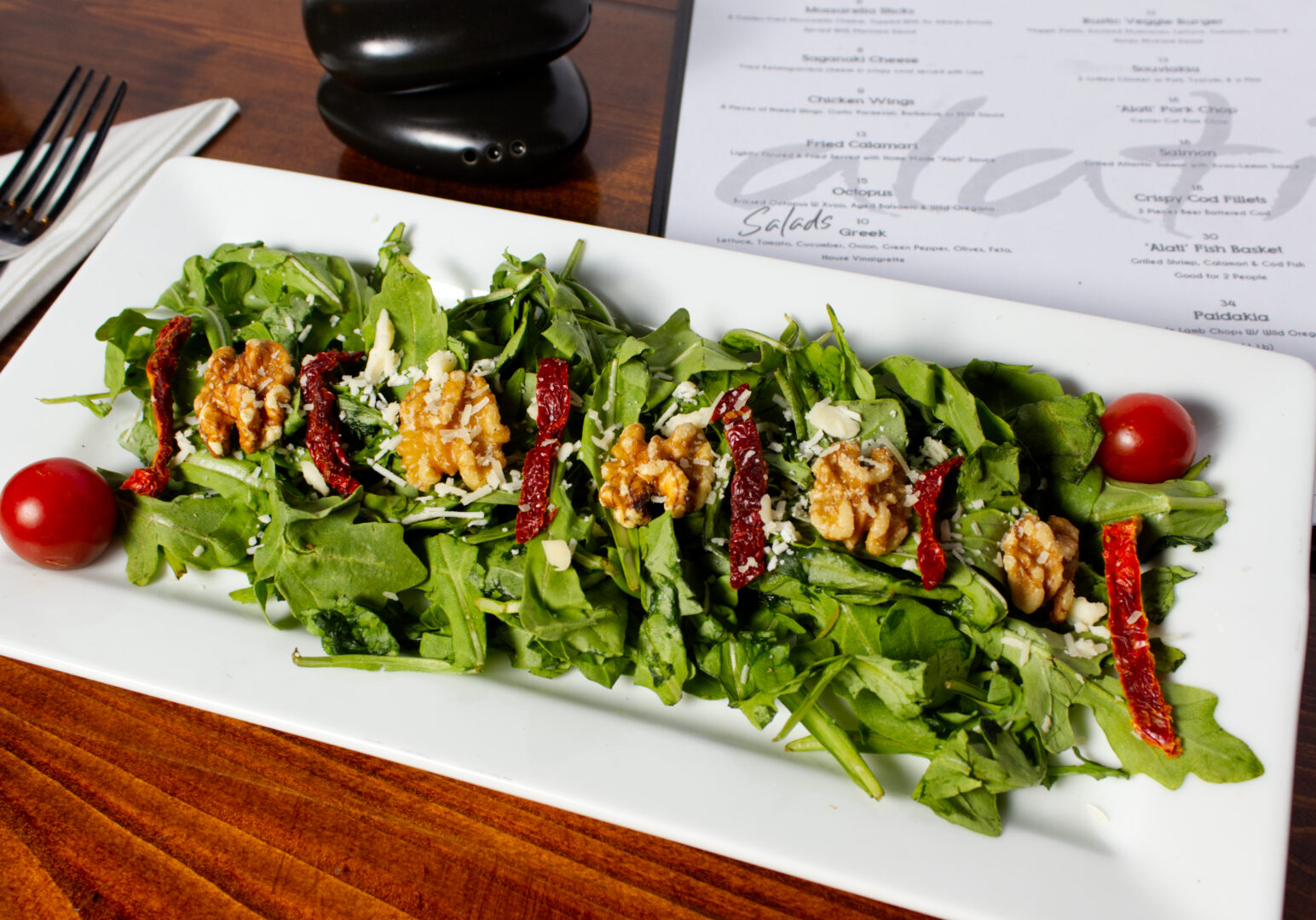 Image_06 Example of Food Photography for DoorDash, Uber Eats, Grub Hub, and any food delivery service app. Food Photo is of a salad on a regtangular white plate. The background is a wood table with a menu from the restaraunt laid out