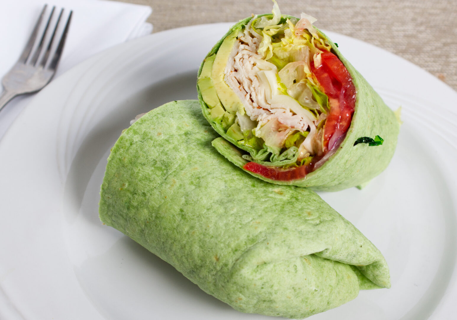 Image_09 Example of Food Photography for DoorDash, Uber Eats, Grub Hub, and any food delivery service app. Food Photo is of a turkey and avocado wrap on a round plate. The wrap is cut in half and positoned so the inside of the contents are on display.