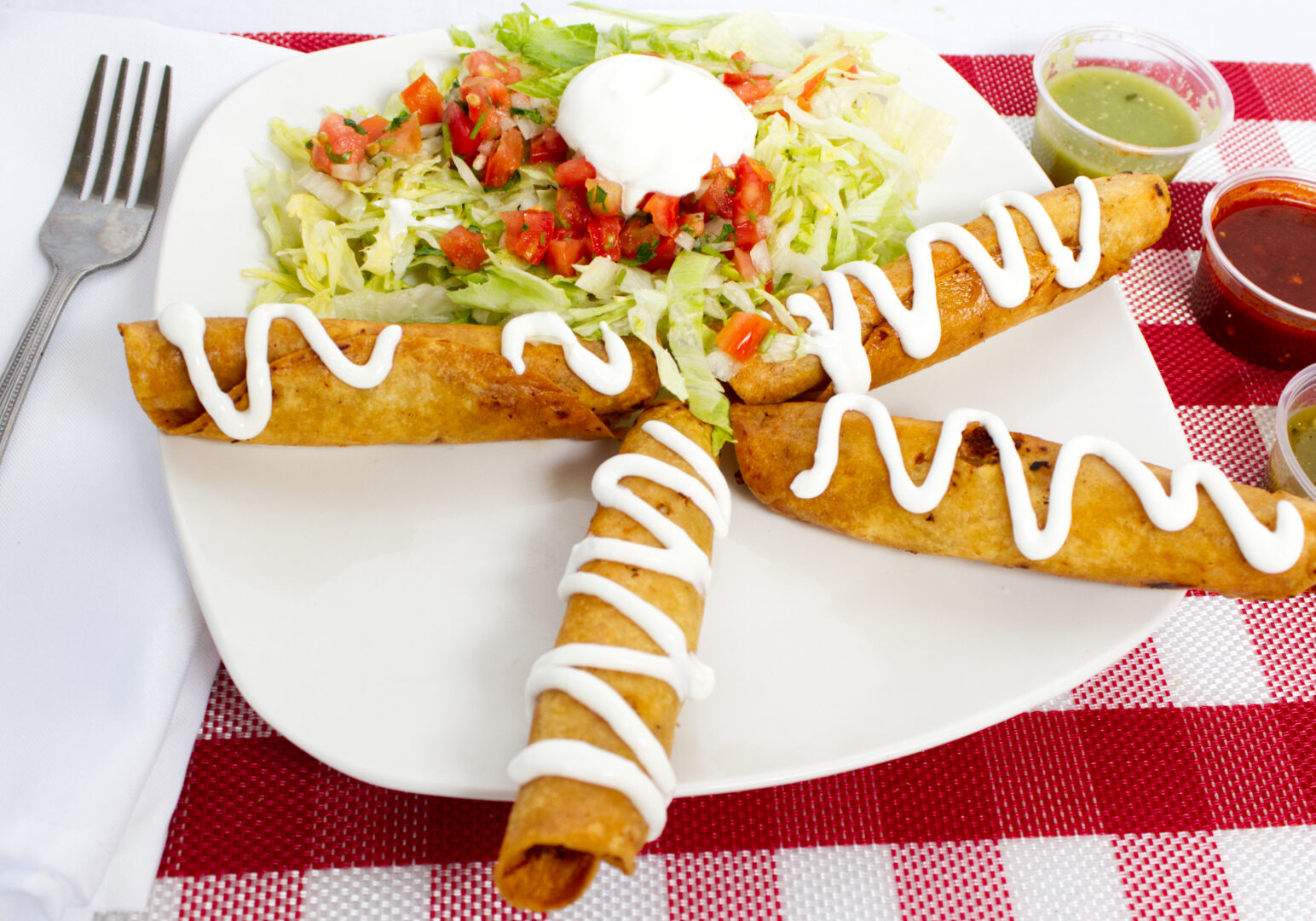 Image_10 Example of Food Photography for DoorDash, Uber Eats, Grub Hub, and any food delivery service app. Food Photo is of 4 Flautas positioned in a star shape on the sqaure plate. Al this and a few accompanying sauces are placed on a red and white striped placematt the looks like a picnic table cloth.